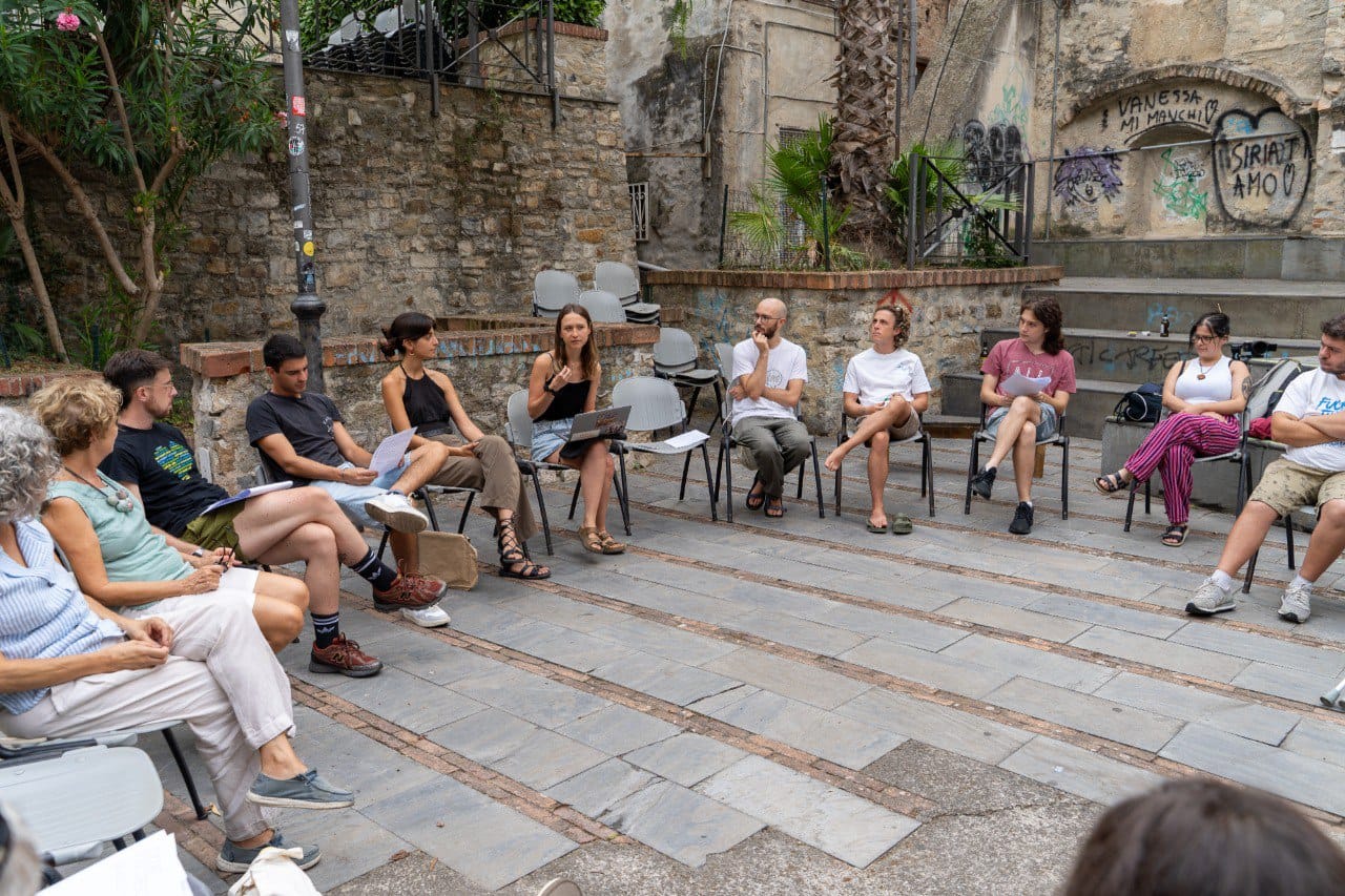 Una decina di persone sedute su delle sedie in cerchio discutono di decrescita, in una piazza del centro storico di Sanremo.